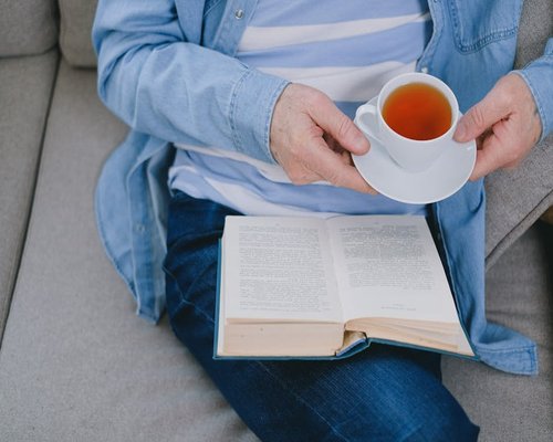 Person relaxing with a book and tea on a cozy sofa